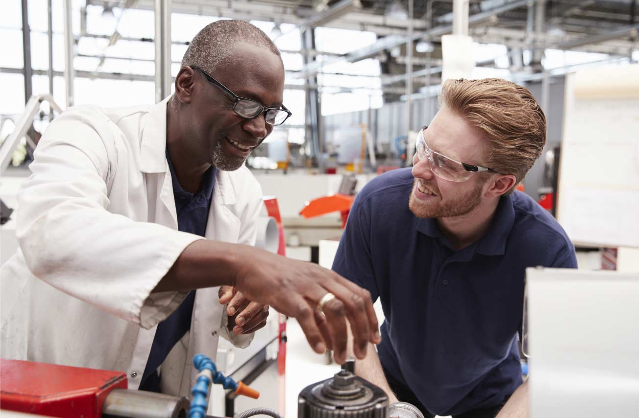 Engineer advising a male apprentice in a factory